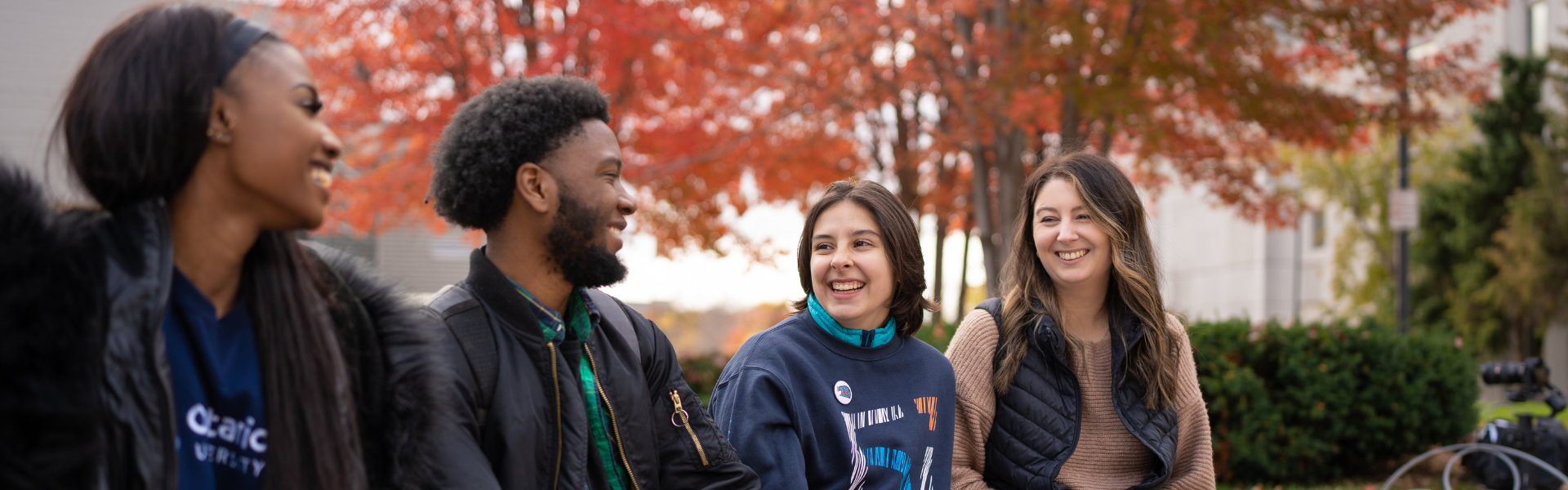 4 students sitting on a bench with trees behind them. 